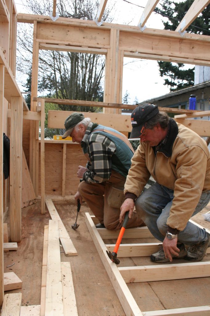 Two builders kneeling to hammer together the timber frame of a new wall
