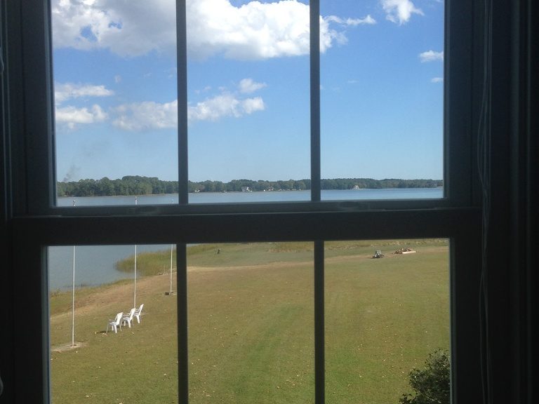A tall paned window looking out over a green lawn towards a calm lake and blue sky